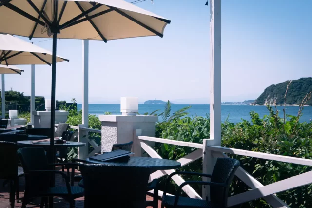 写真：晴れた日の海辺のレストランカフェのテラス席。水平線の向こうに江ノ島が見える。
