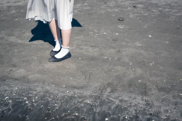 写真：砂浜に立っている、スカートをはいた女性の足