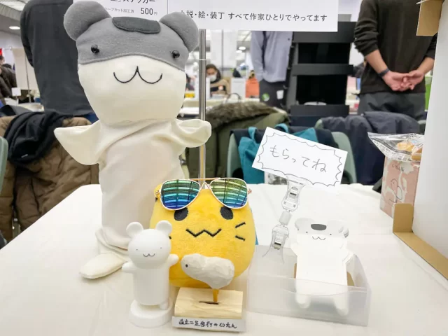 写真：2026/1/18 文学フリマ京都10 シーサイドブックス 卓上 ねずみちゃんマペットと名刺、イタリさんにモデリング・出力していただいたねずみちゃん3Dプリンタ製フィギュア、うえのさんが作成された木彫りのとりたん、サングラスをかけたにゃんぷっぷー(blobcat)