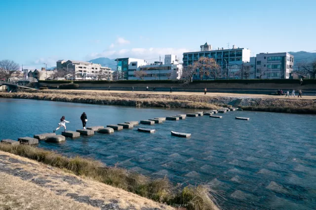 写真：鴨川の飛び石を渡る2人の人物を遠くから撮影